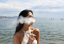 Vaping and Cannabis: What You Need To Know woman wearing white sleeveless top smoking tobacco while standing near blue sea under white and blue skies during daytime