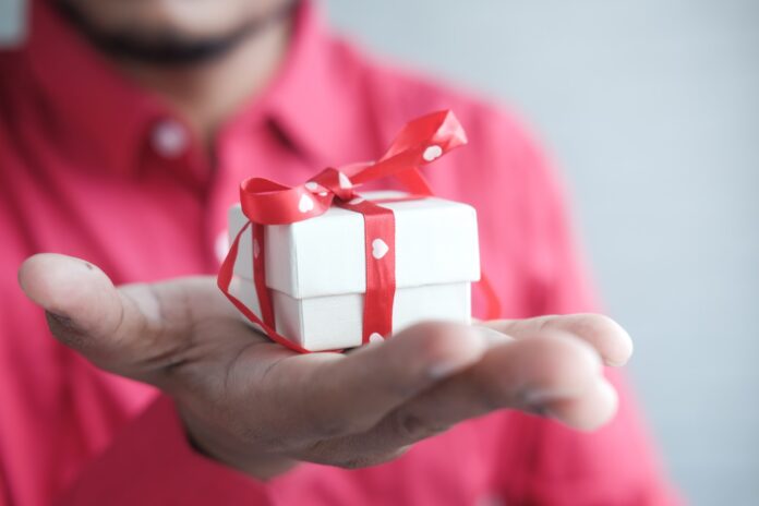 Photo by Towfiqu barbhuiya a man holding a white gift box with a red ribbon