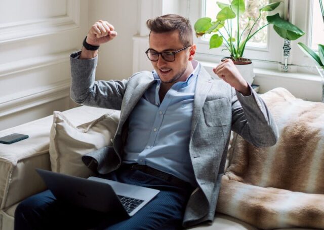 Happy Man Sitting with Laptop Clenching Fists